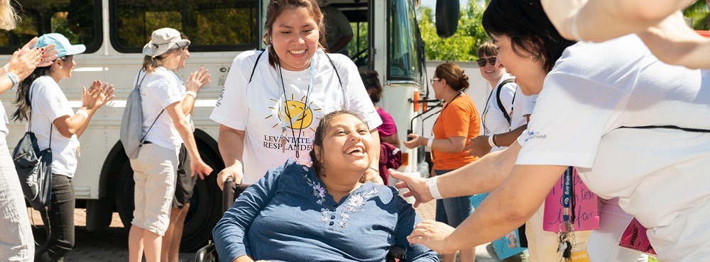 A woman in a wheelchair is being greeted by a group of people.