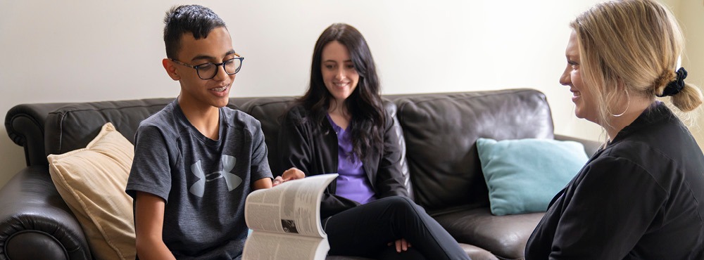 Three people sitting on a couch reading a a book.