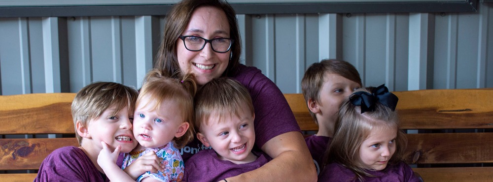 A woman in a purple shirt with her children on a bench.