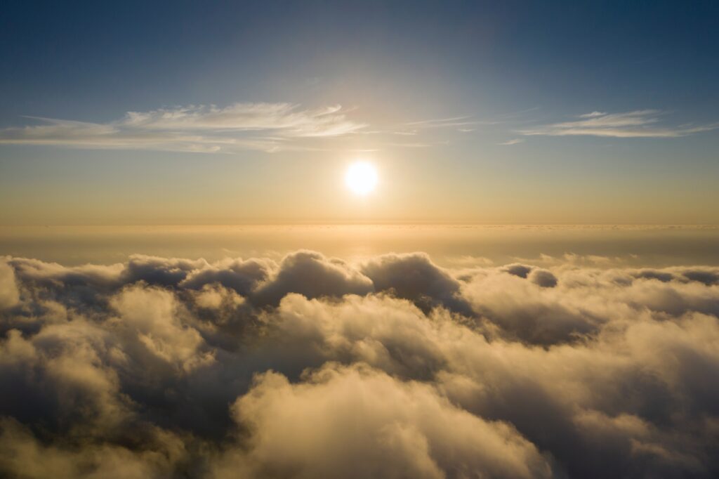 A photo from above clouds with blue sky and the sun shining.