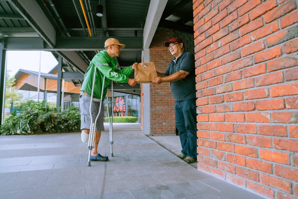 A man on crutches with an amputated food taking a paper bag from another man.