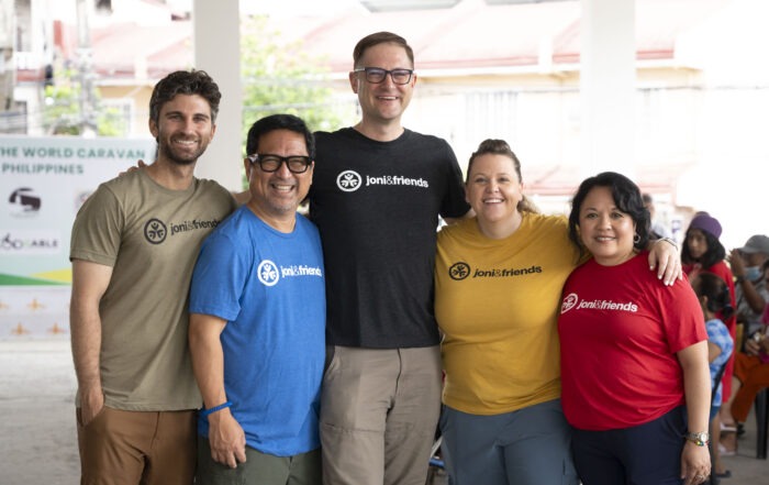 A group photo of Evalerie with four other Joni and Friends employees. They're all wearing different colored Joni and Friends tshirts.