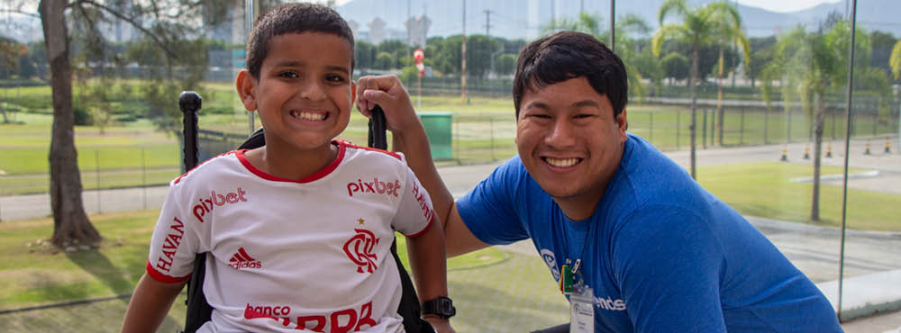 A boy smiling in his wheelchair and an intern smiling next to him