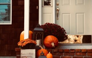 A front doorstep with pumpkins and mums on the steps.