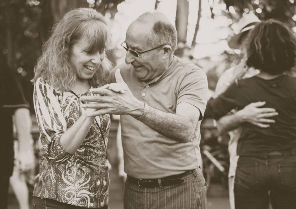 A black and white photo of an elderly couple dancing together and smiling.