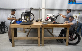 A photo of men working on Wheelchairs at our newest Wheelchair Restoration Center in El Salvador. One of the men is using a wheelchair for mobility.