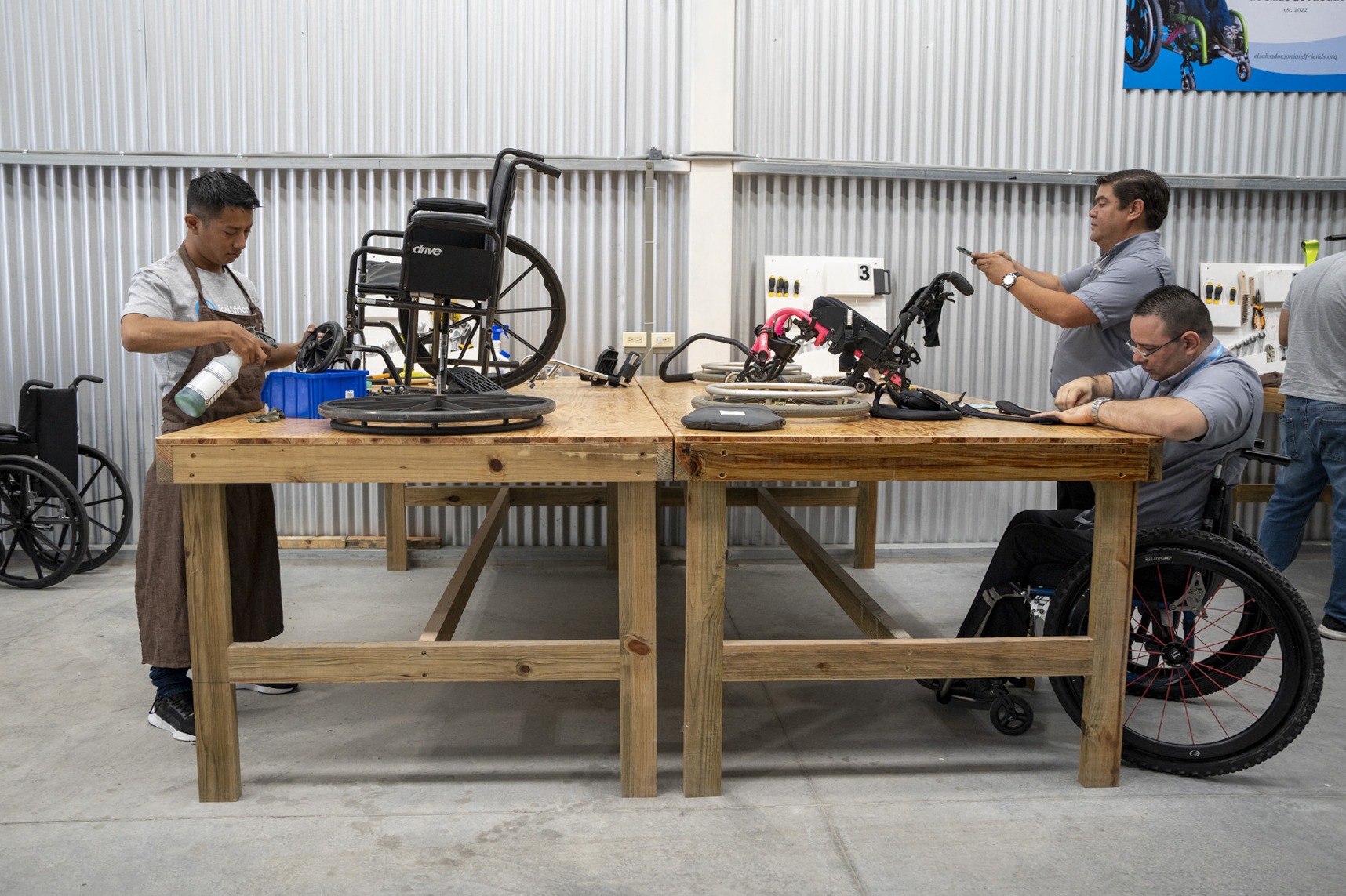 A photo of men working on Wheelchairs at our newest Wheelchair Restoration Center in El Salvador. One of the men is using a wheelchair for mobility.