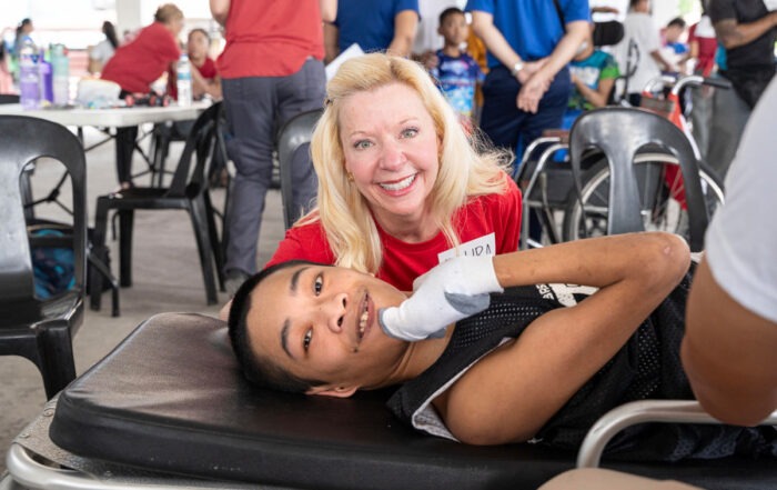 A close up photo of Jimly and Laura both smiling at the camera. Jimly is lying down on a stretcher while Laura is kneeling beside him.