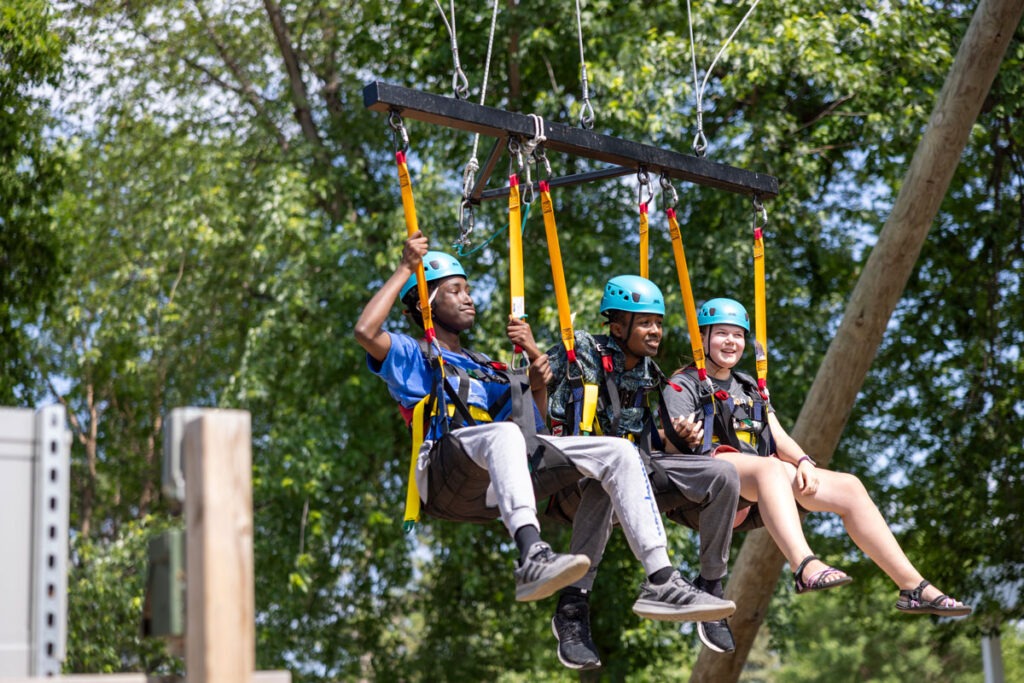 A picture of three boys on what appears to be three-person a zip-line seat.