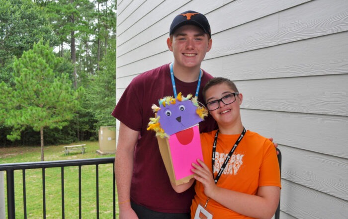 A picture of Keegan and his Joni and Friends buddy smiling at the camera. Keegan is holding up a puppet made out of a paper bag.