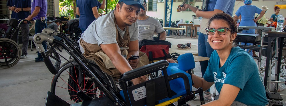 Two volunteers make adjustments to a wheelchair at a Wheels for the World outreach.