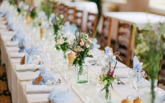 A picture of a beautifully decorated table for a wedding feast. It has a white linen tablecloth on it and bouquets of wildflowers.
