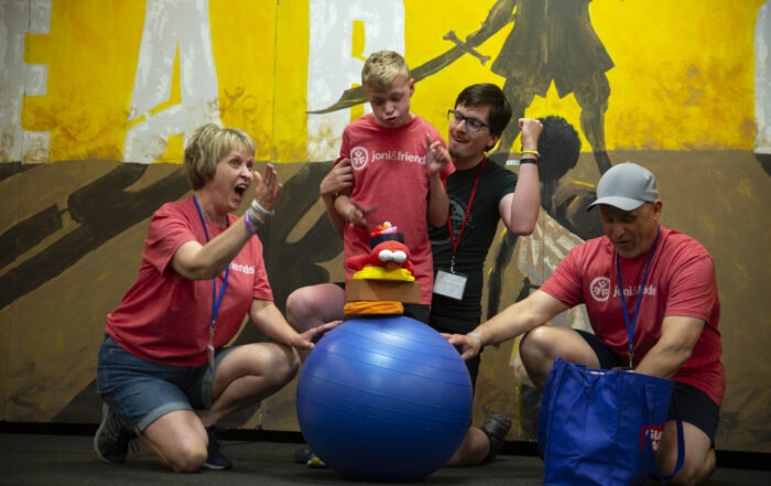 A picture of Cole playing with three Joni and Friends buddies with a large blue exercise ball and what appears to be a puppet.