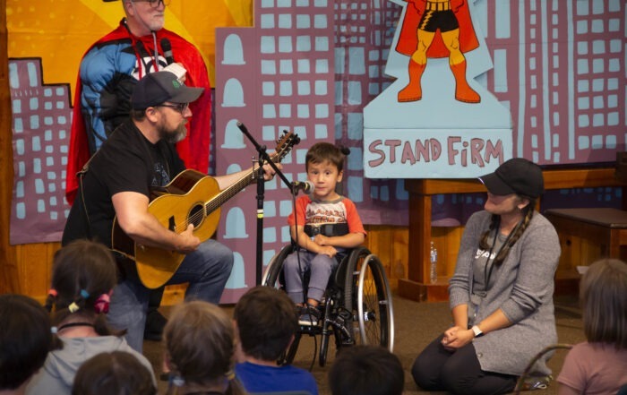 A picture of Jamie singing at the Joni and Friends Family Retreat talent show as he's seated in his wheelchair and smiling at the camera.