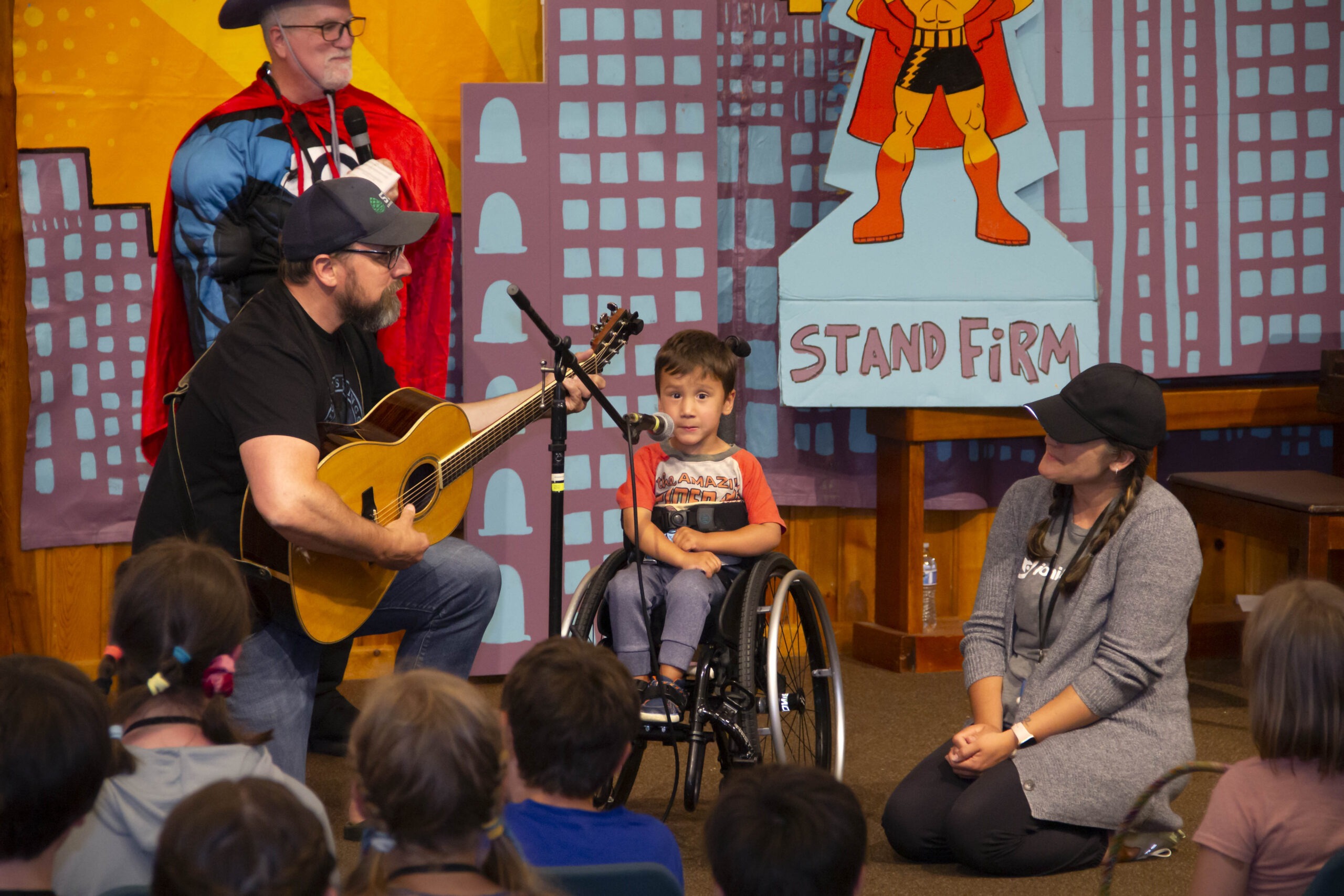 A picture of Jamie singing at the Joni and Friends Family Retreat talent show as he's seated in his wheelchair and smiling at the camera.