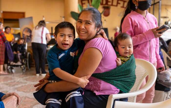 A photo of Abel and his mom and his baby brother all sitting in a chair and smiling at the camera.