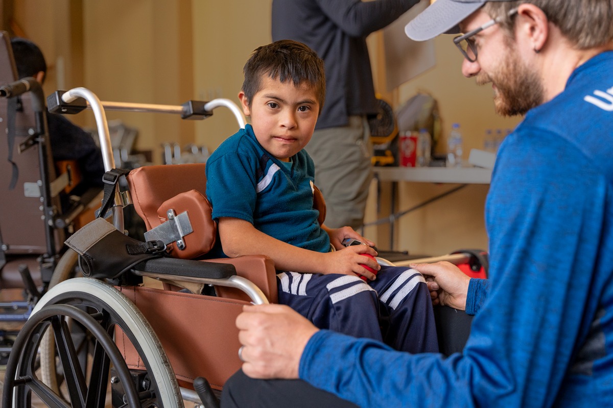 A photo of Abel seated in his new wheelchair with a Joni and Friends volunteer adjusting the wheelchair.