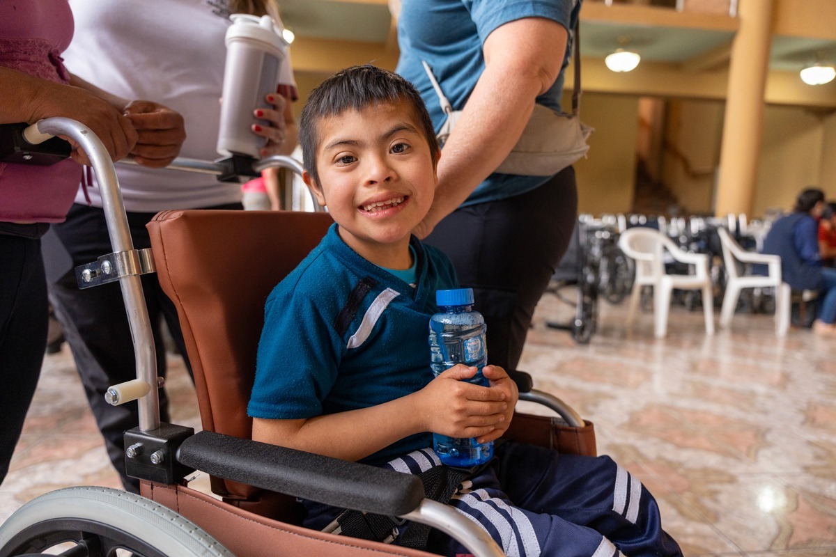 A photo of Abel smiling at the camera in his brand new wheelchair with a water bottle in his hand.