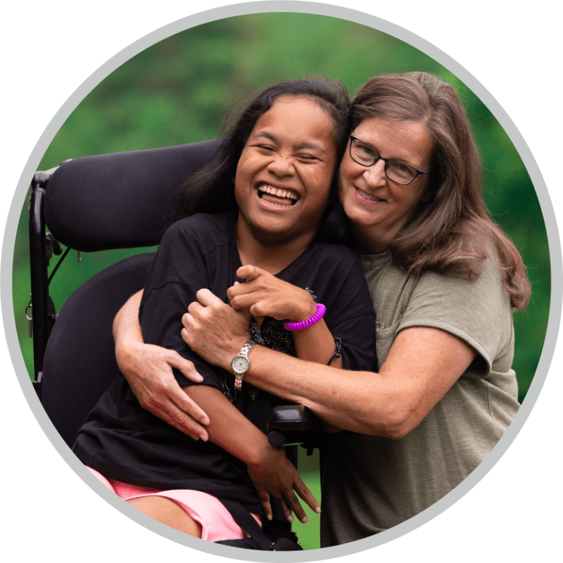 A girl in a wheelchair enjoying so much as she is being hugged by a woman next to her.