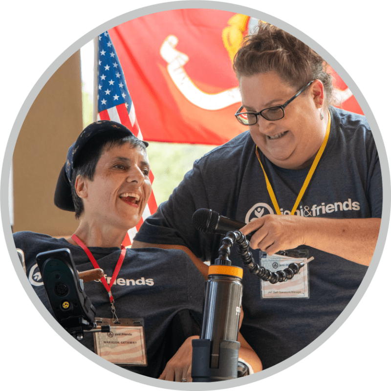A woman in a wheelchair next to another woman who is adjusting the microphone for her.