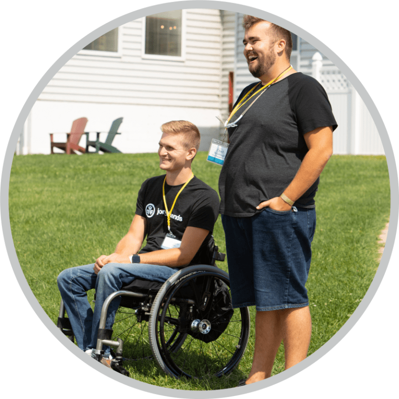 A man using a wheelchair next to another man standing beside him.