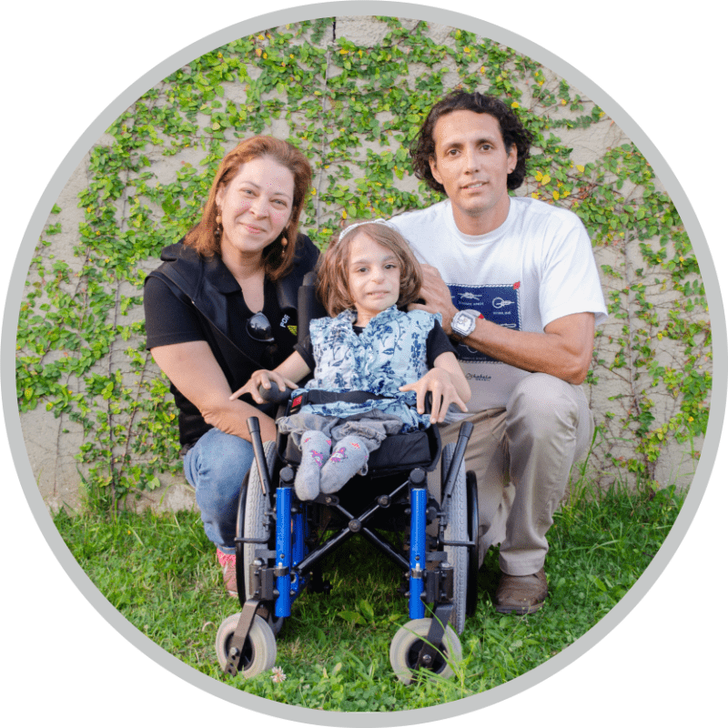 A mother, a father, and their child in a wheelchair smiling and posing for the camera. 