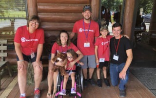 A group photo of Chris and Kayla at Knoxville Family Retreat with their children Morgan and Holsten. All are wearing their red Joni and Friends t-shirts. Little Morgan is seated in a small, pink detailed wheelchair.