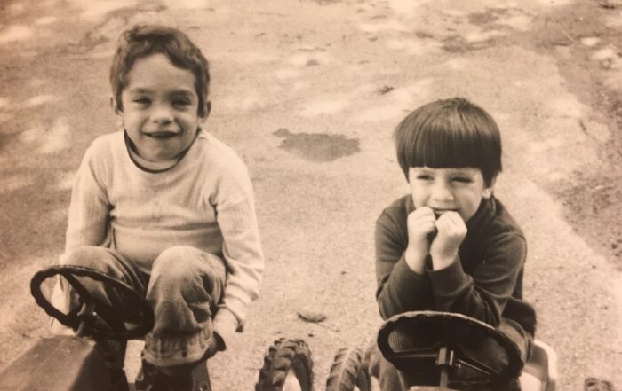 A black and white photo of Jerry and Mike on tricycles when they were little boys smiling at the camera.