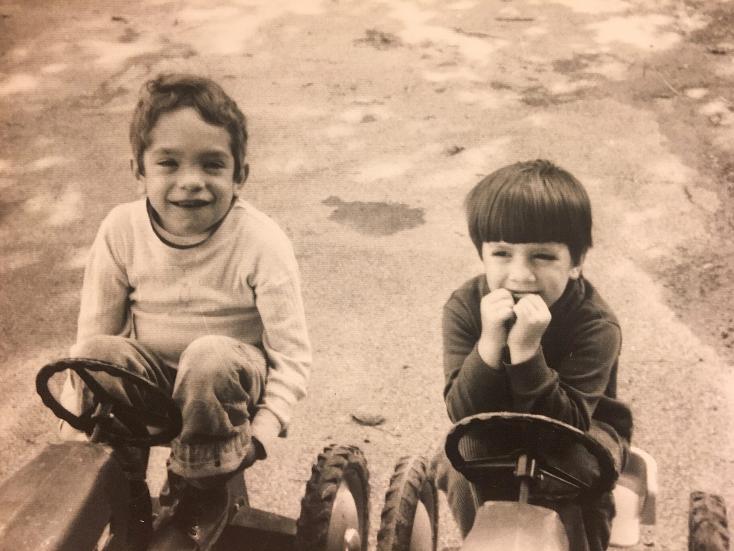 A black and white photo of Jerry and Mike on tricycles when they were little boys smiling at the camera.