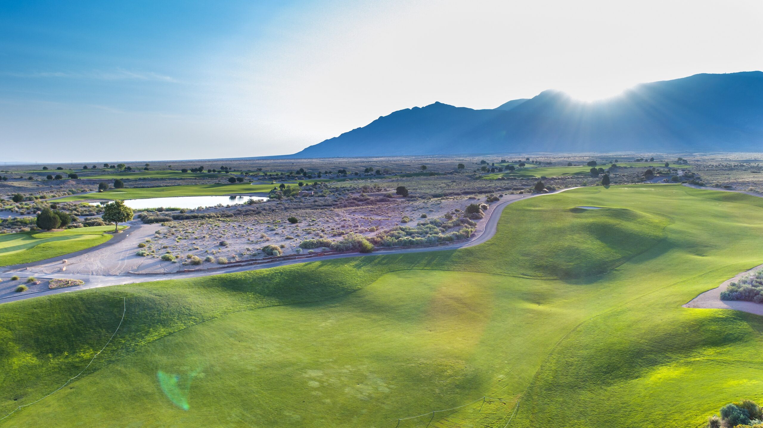 A photo of a golf green and the sun peaking over the mountains