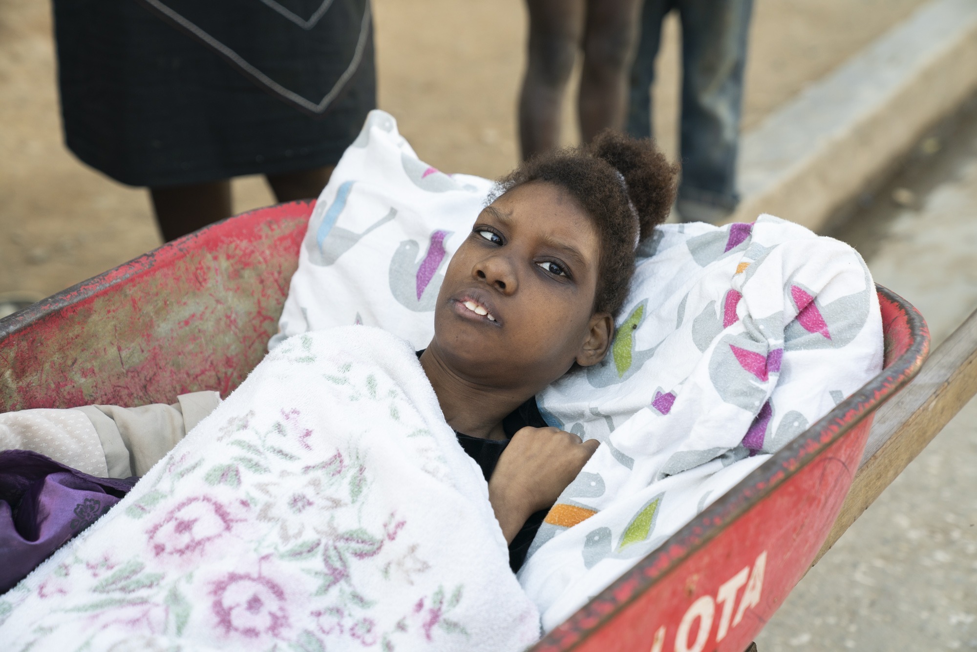 A picture of a young woman lying down in a wheelbarrow with her eyes on the camera.