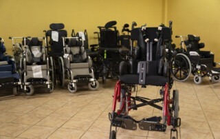 A picture of a small wheelchair with other wheelchairs lined up behind it against a bright yellow wall.