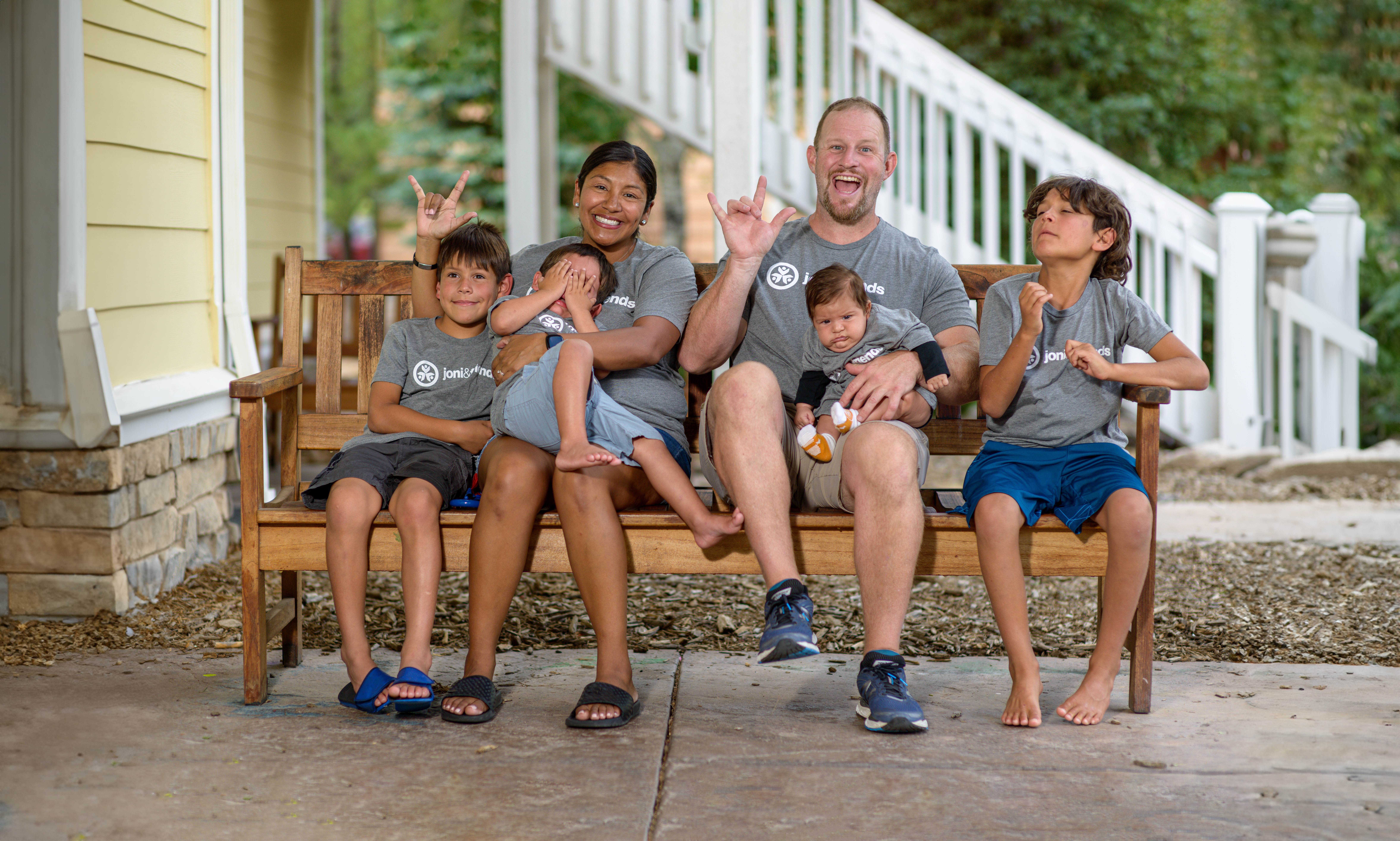 A group photo of Enoch and his family. He is sitting on a bench with his three siblings and his mom and dad, all are wearing grey Joni and Friends t-shirts and smiling at the camera.