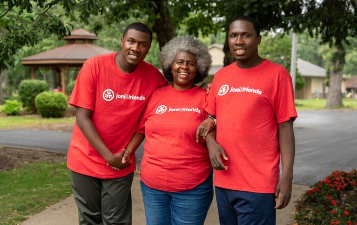 A group picture of Tyrone, Caleb and Muriel standing arm in arm with their red Joni and Friends shirts on, all are smiling at the camera.