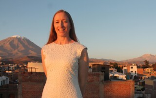 A picture of Christine smiling at the camera in a white dress with snow-capped mountains behind her.