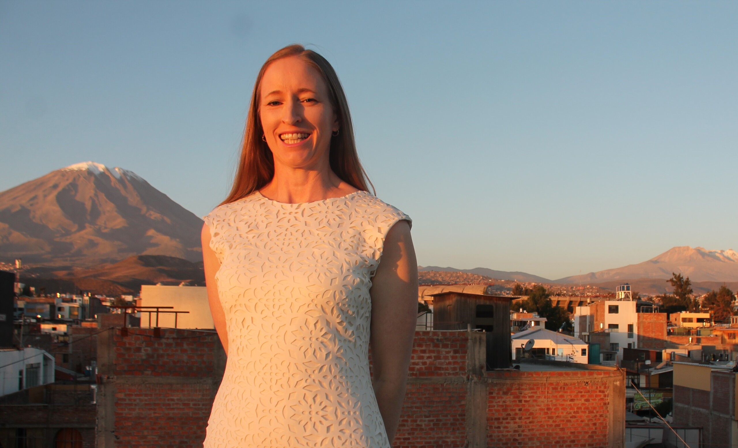 A picture of Christine smiling at the camera in a white dress with snow-capped mountains behind her.