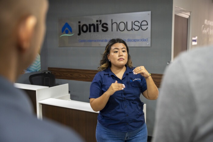 Joni's House staff member demonstrating sign language with Joni's House sign in the background.