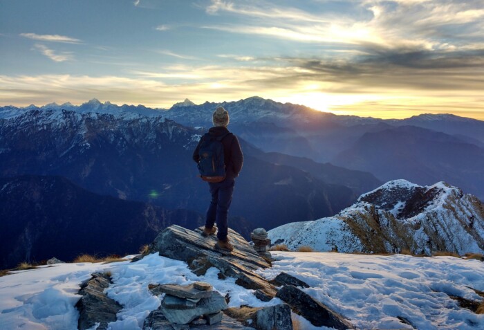 A man standing on the side of a snowy mountain staring at a sunset.