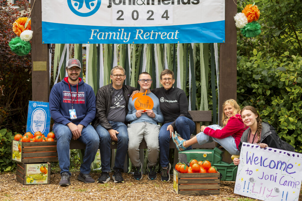 A photo of Trevor and his family sitting together in front of a "Joni and Friends 2024 Family Retreat" banner, smiling and posing for the camera.