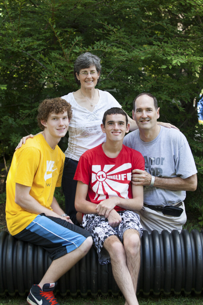 Portrait of the Doran family posing together outdoors, smiling against a backdrop of lush green trees.