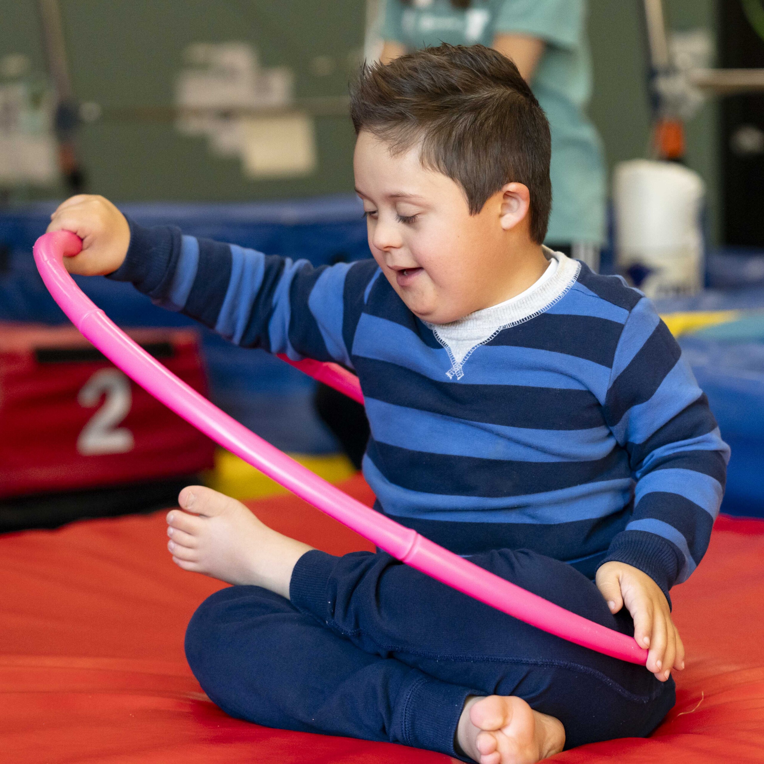 A child sitting on the ground, playing with a hula hoop.