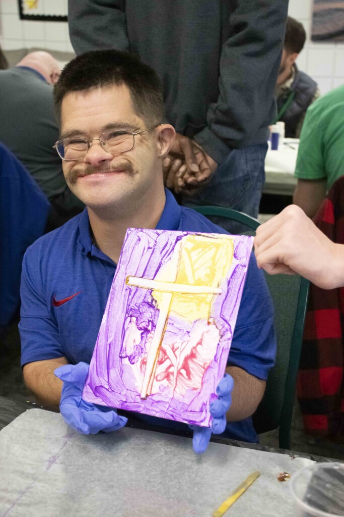 BJ smiling and showing his colorful painting of a cross.