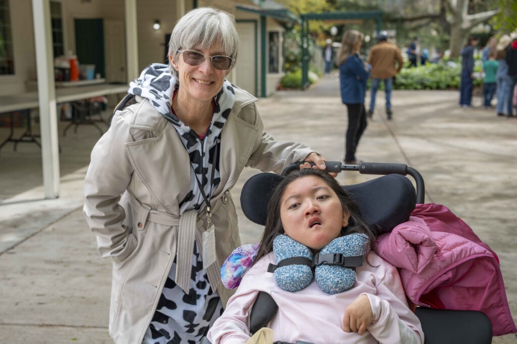 Kathy is smiling and standing next to a girl who is in a wheelchair.