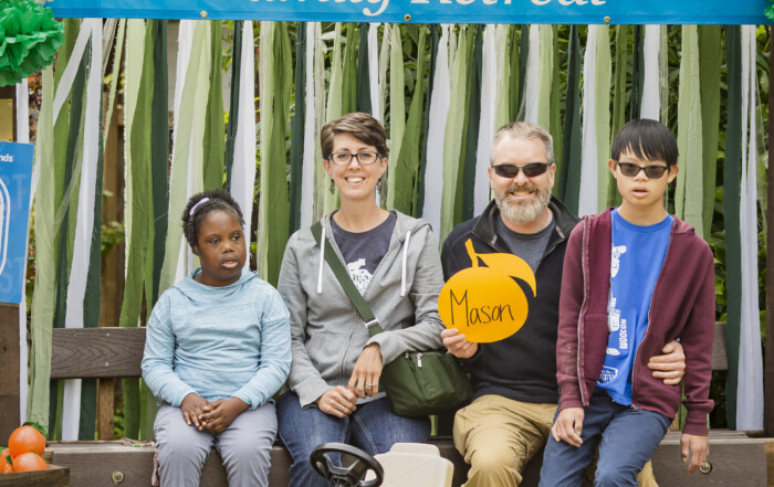 Becky and Nathan with their two youngest children, Lydia and Caleb, sitting and smiling at the camera, with a "Joni and Friends 2024 Family Retreat" banner in the background.