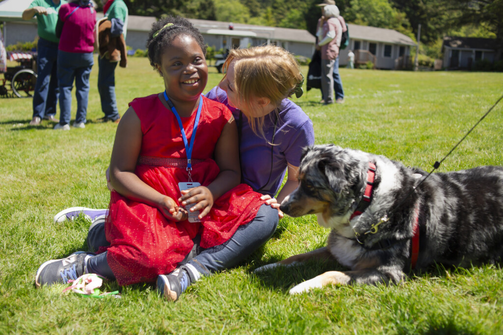 A volunteer at Joni and Friends and Lydia sitting on the grass while talking to each other with a dog next to them.