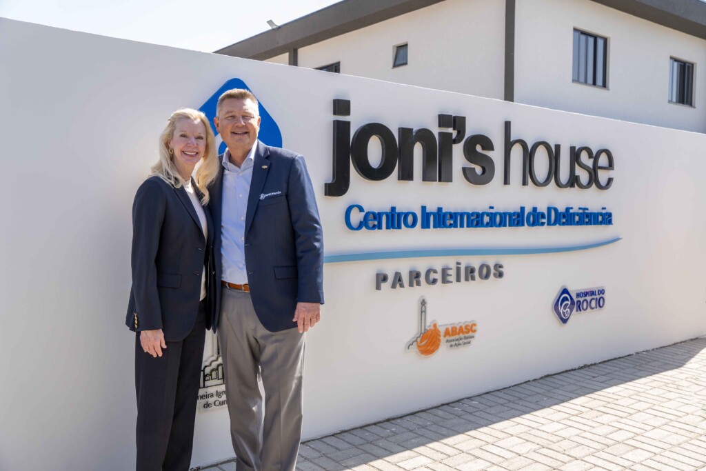 Laura Gardner and Steve Bundy standing next to a sign that reads "Joni's House Centro Internacional de Deficiencia,"featuring the logos of partner organizations: Primeira Igreja Batista de Curitiba, ABASC (Associação Batista de Ação Social), and Hospital do Rocio, positioned underneath.