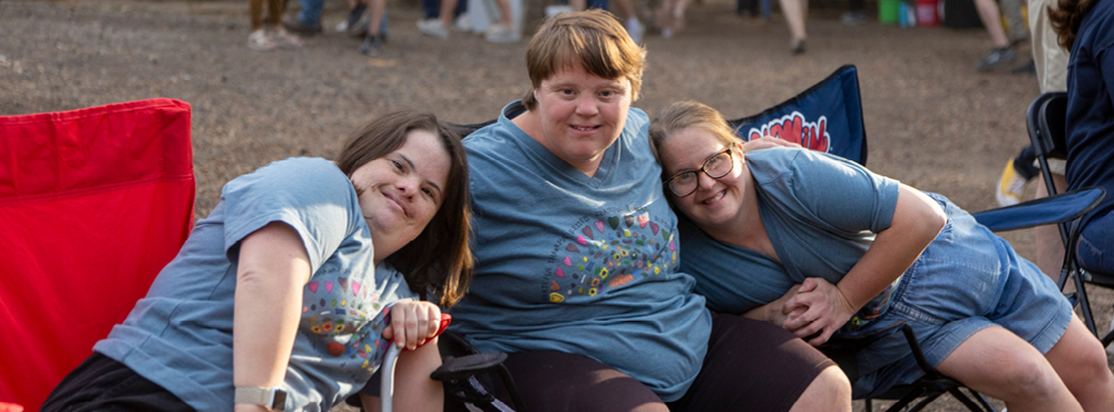 Three attendees sitting and smiling at the camera and enjoying their time at the Barnyard Dance event.