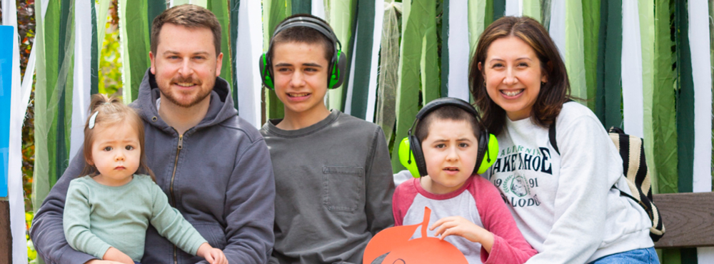 A family of four, consisting of two adults and three children, are smiling and posing happily for the camera. They are dressed casually and appear to be enjoying their time at a Family Retreat event.