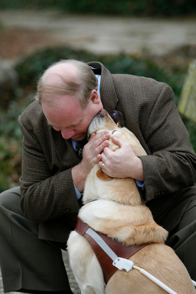 Michael Hingson is petting and hugging his guide dog, Roselle, who is giving him affectionate kisses on the face.