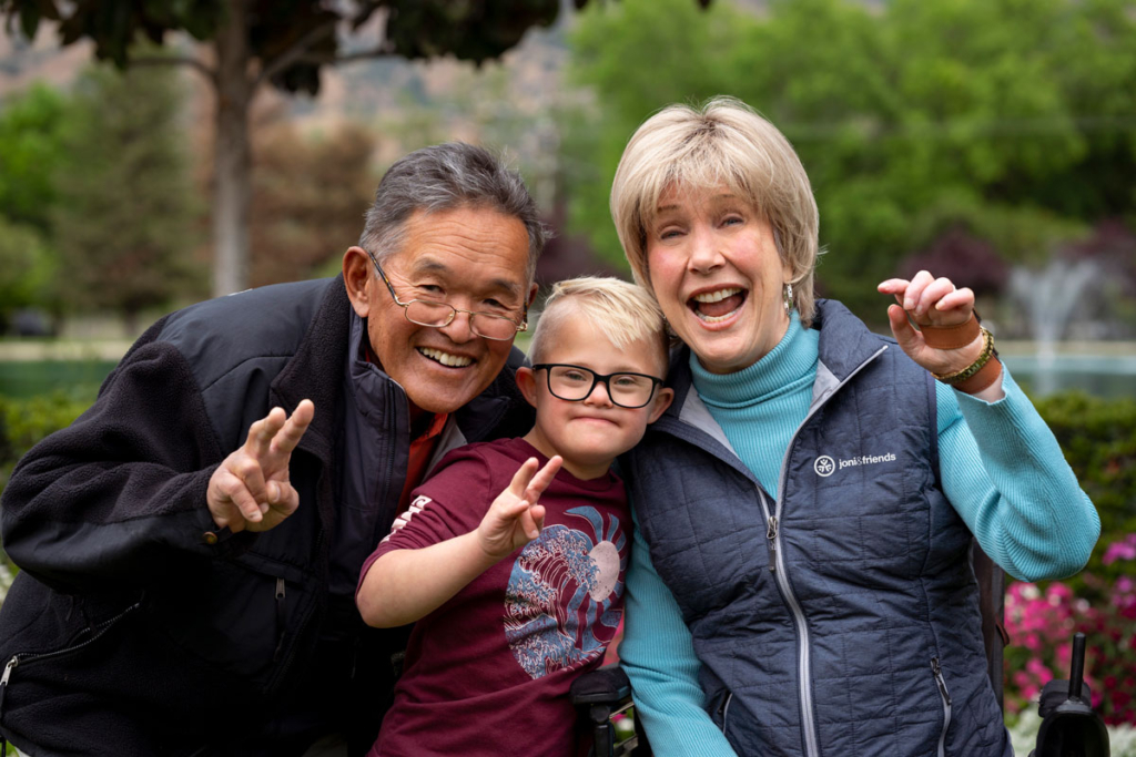 Joni and Ken are smiling and happy as they pose for the camera, with a young boy positioned between them. All three are beaming and appear joyful, creating a warm and cheerful scene.